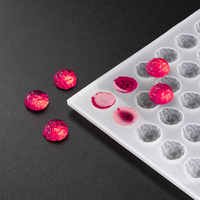 A silicone mold with a 3D shape resembling a brain, used for depositing candy in that shape. The mold is shown alongside a few candies that have been made using this mold.