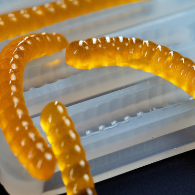 100%platinumsiliconemoldcloseup5mLGummyWormDepositorCandyGummyMoldPlain66cavitiesorangegummywormsblackgroundtranslucentmold
