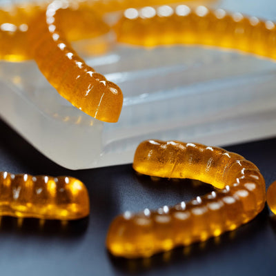 100%platinumsiliconemoldcloseupcorner5mLGummyWormDepositorCandyGummyMoldPlain66cavitiesorangegummywormsblackgroundtranslucentmold